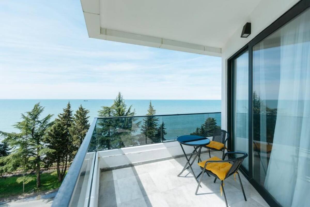 Een balkon met uitzicht op zee, twee stoelen en een glazen deur.