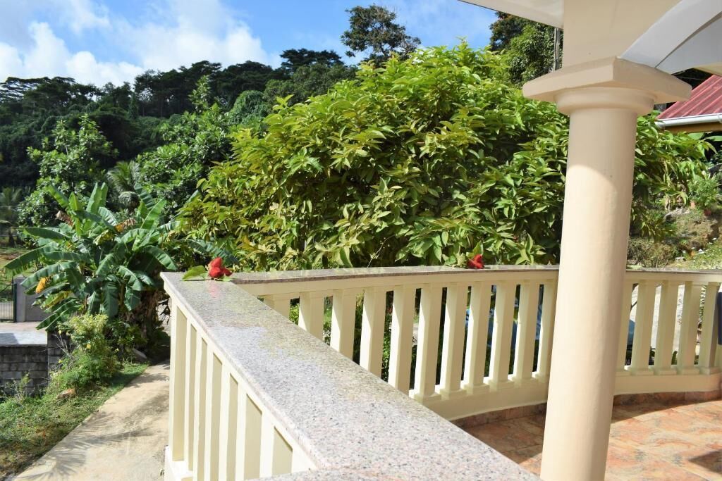 A balcony with a railing, a stone pathway, and lush greenery in the background.
