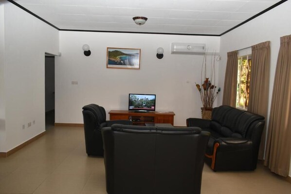 Un salón con televisor de pantalla plana, dos sofás de cuero negro, una mesa de centro de madera y un cuadro en la pared.