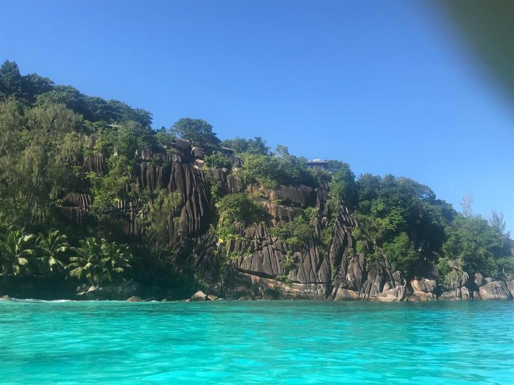 A coastal landscape with clear turquoise waters, rocky cliffs, and dense greenery.