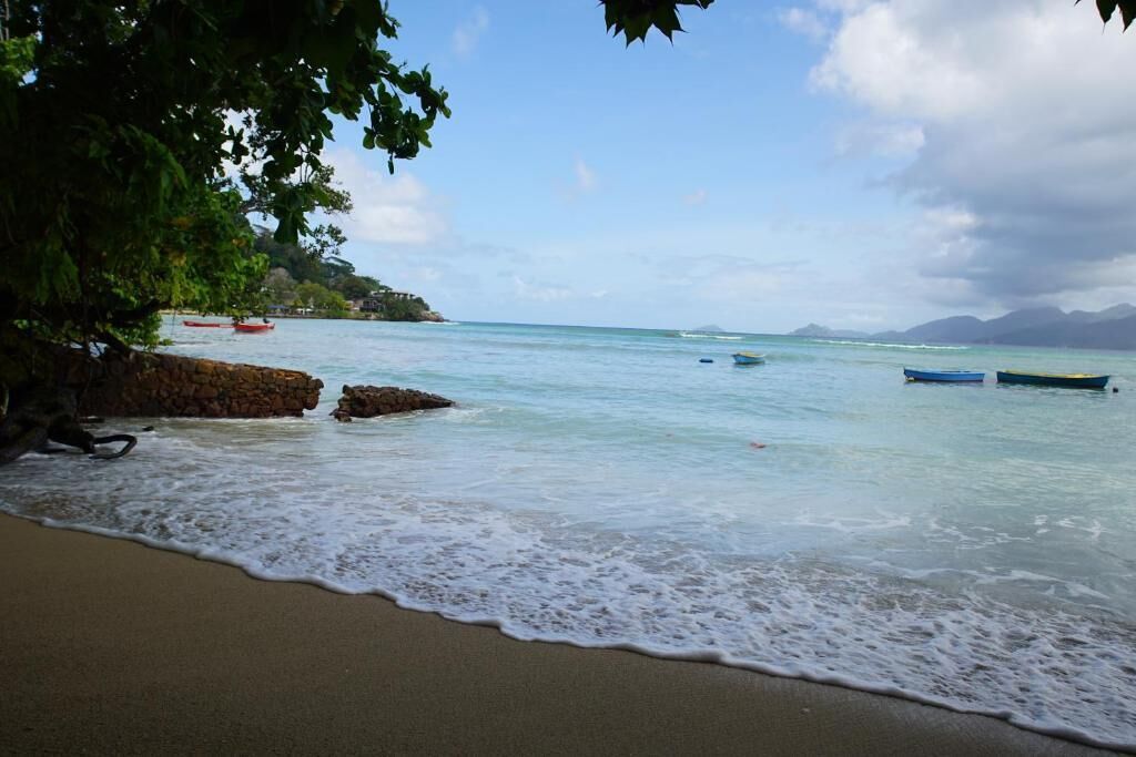 Una playa con aguas tranquilas, barcos y un litoral rocoso.