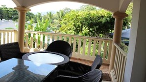 Un espace extérieur abrité, aménagé avec une table et des chaises, une rambarde blanche et une végétation luxuriante en arrière-plan.