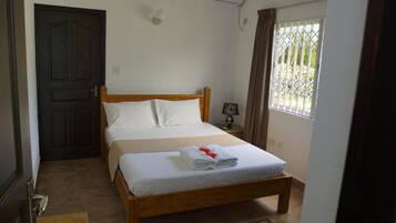 A hotel room with a bed, a door, an air conditioning unit, a nightstand, and a window with curtains.