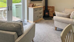 Ein gemütliches Wohnzimmer mit Kamin, einem an der Wand montierten Fernseher und Blick durch die Glastür ins Freie.