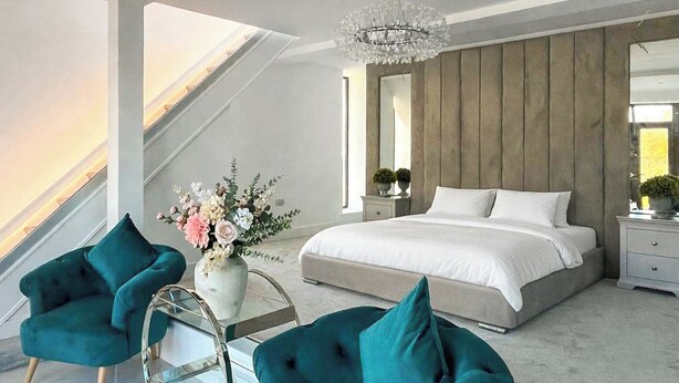 Ein modernes Schlafzimmer mit einem großen Bett, zwei smaragdgrünen Sessel, einem Glastisch und einer Kronleuchter.