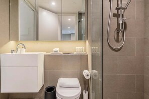 Un baño moderno con cabina de ducha de vidrio, lavamanos blanco y retrete.