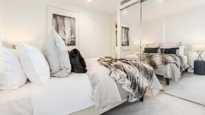 Una camera da letto moderna con un letto, cuscini, una coperta, uno specchio e opere d'arte alle pareti.