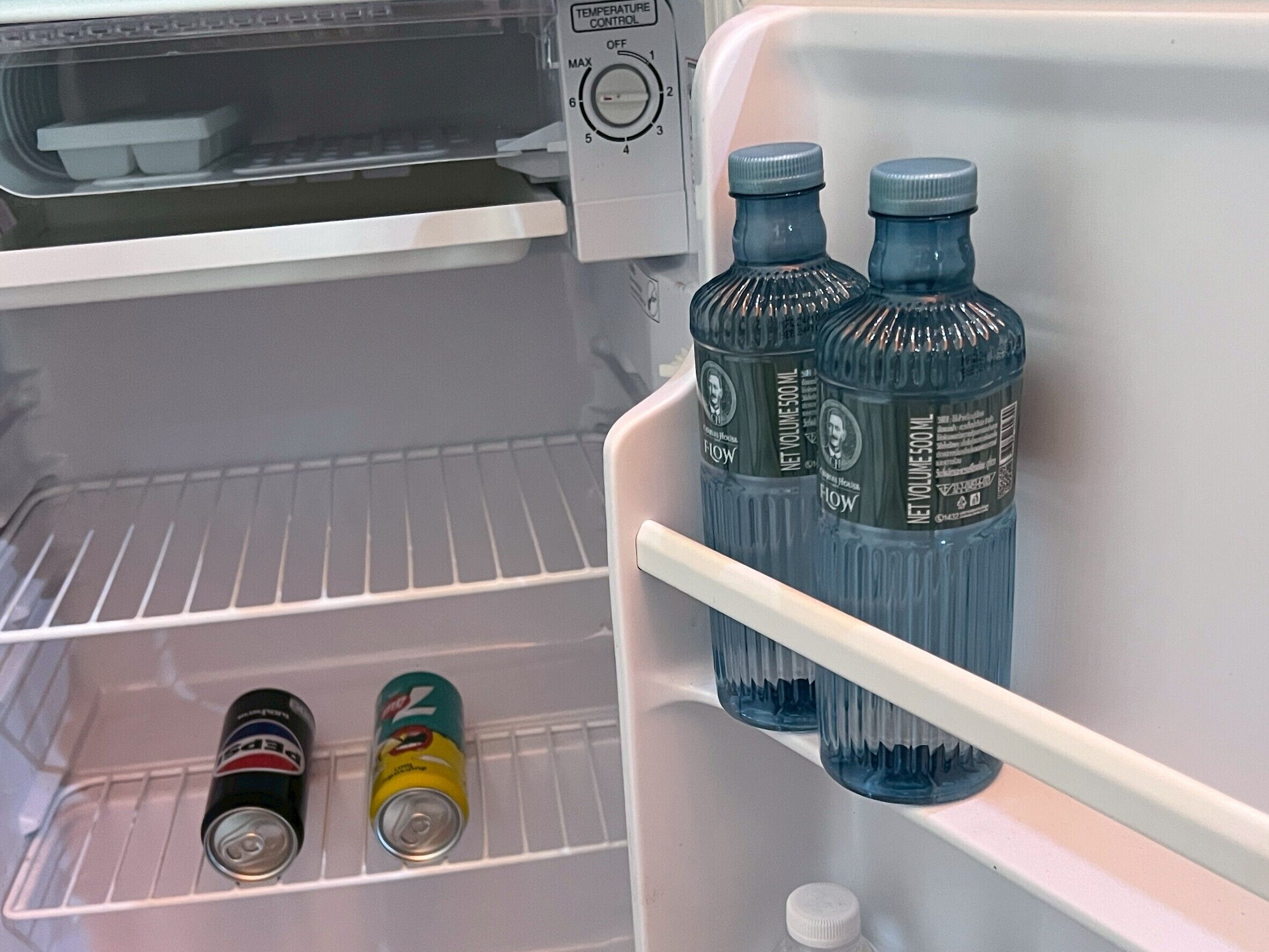 A refrigerator with a temperature control dial, two bottles of water, and two cans of soda.