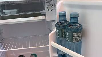 A refrigerator with a temperature control dial, two bottles of water, and two cans of soda.