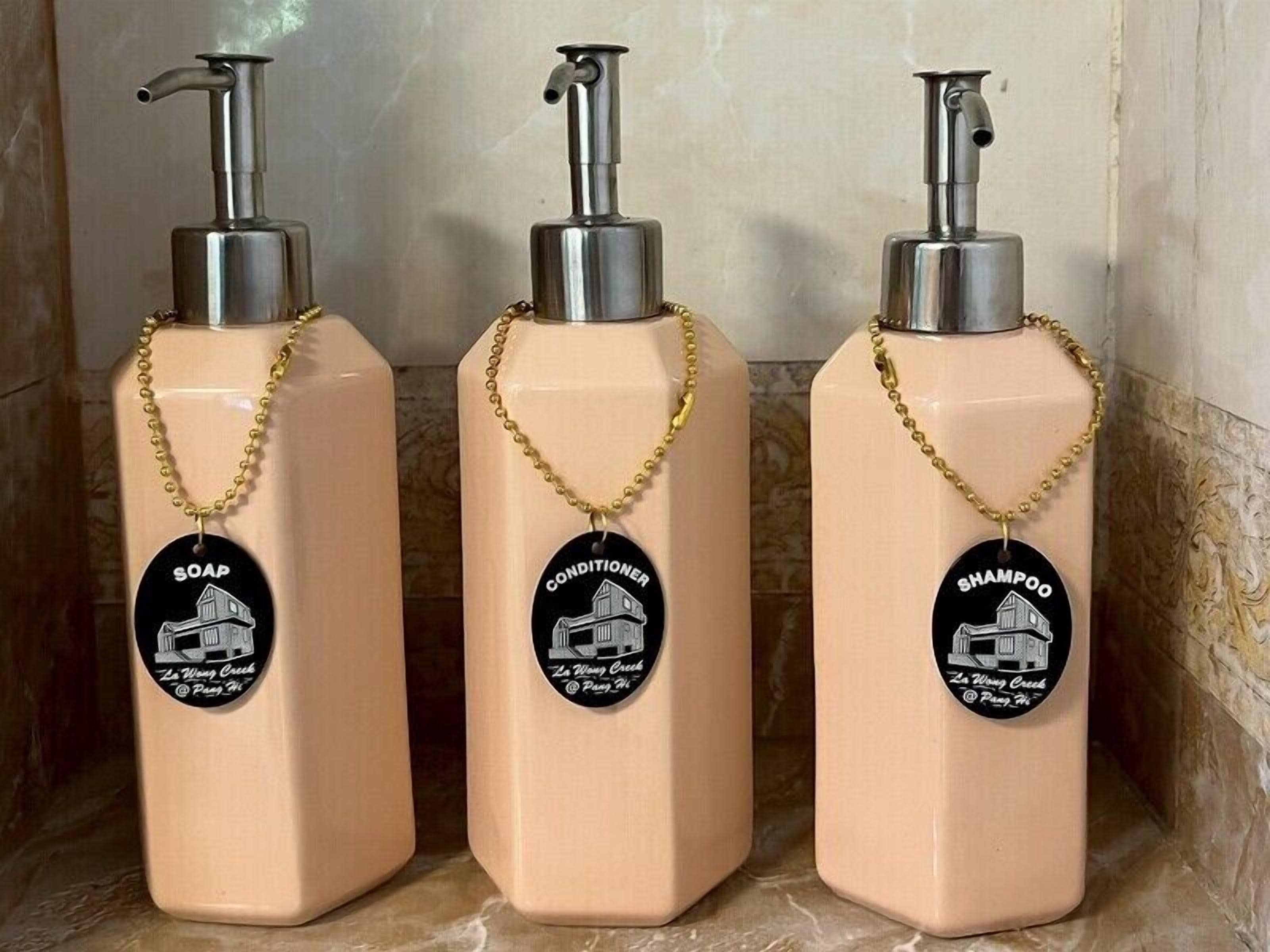 Three bottles of liquid soap, conditioner, and shampoo with pumps and gold chains.