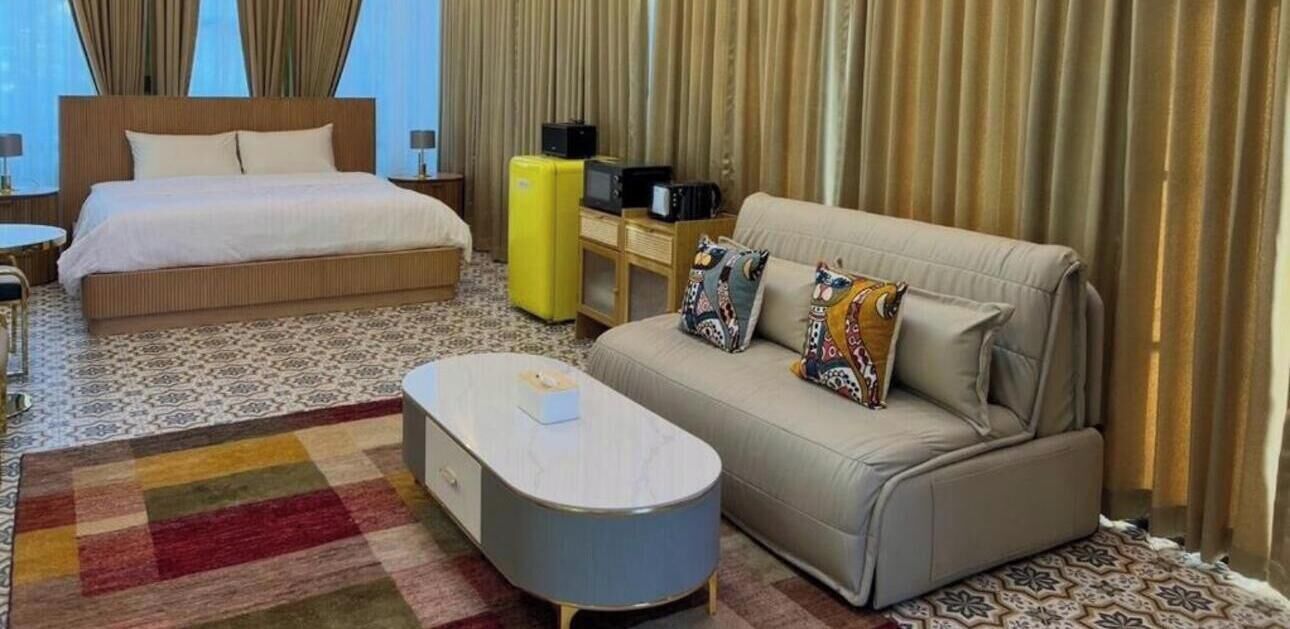 Una habitación de hotel con cama, sofá, mesa de centro y una mesita de noche con lámpara.