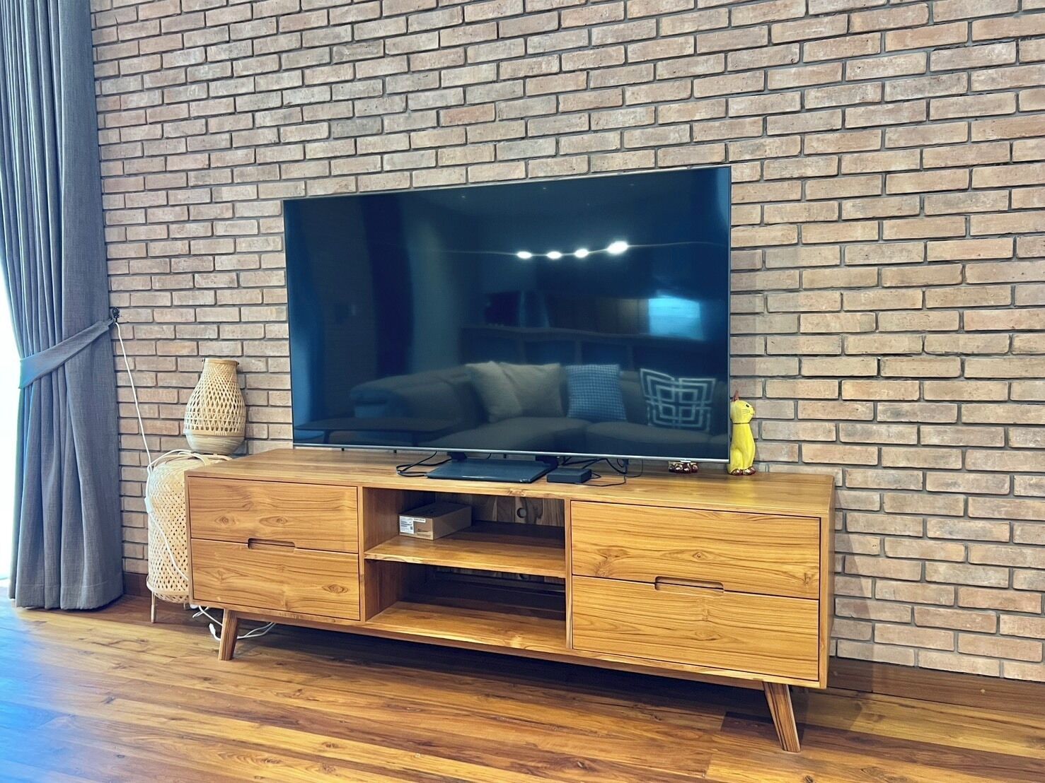 A modern living room with a brick wall, a flat-screen TV on a wooden TV stand, a sofa, and a decorative lamp.