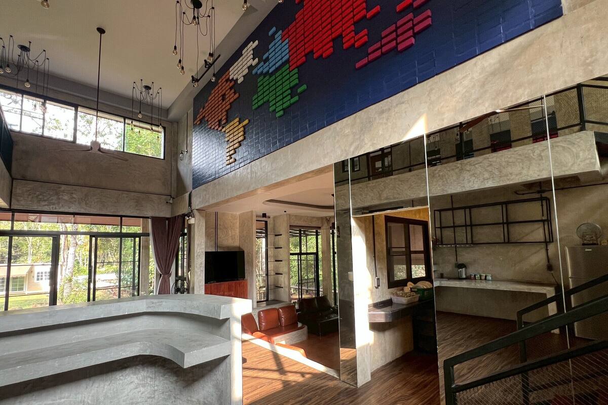 Een ruim interieur met een hoge plafond, grote ramen, een moderne keuken en een trap.