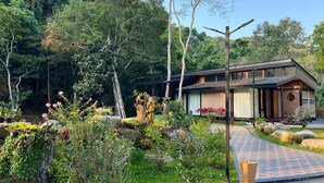 A modern house with a brick exterior, surrounded by lush greenery and a paved pathway. - La Wong Creek at Pang Hi (Doi Saket)