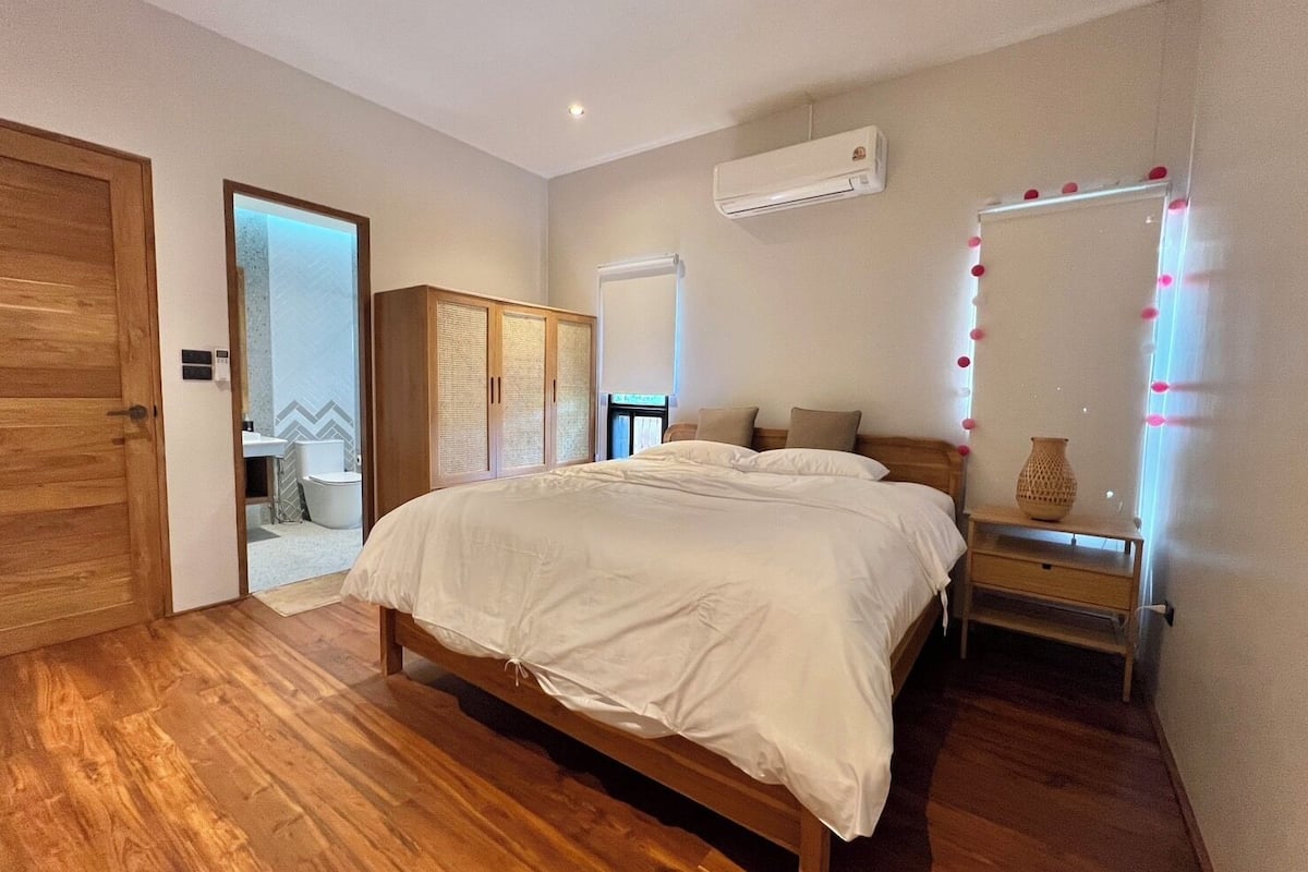 Een slaapkamer met een houten bed, een kledingkast, een airconditioning en een kaptafel met verlichting.