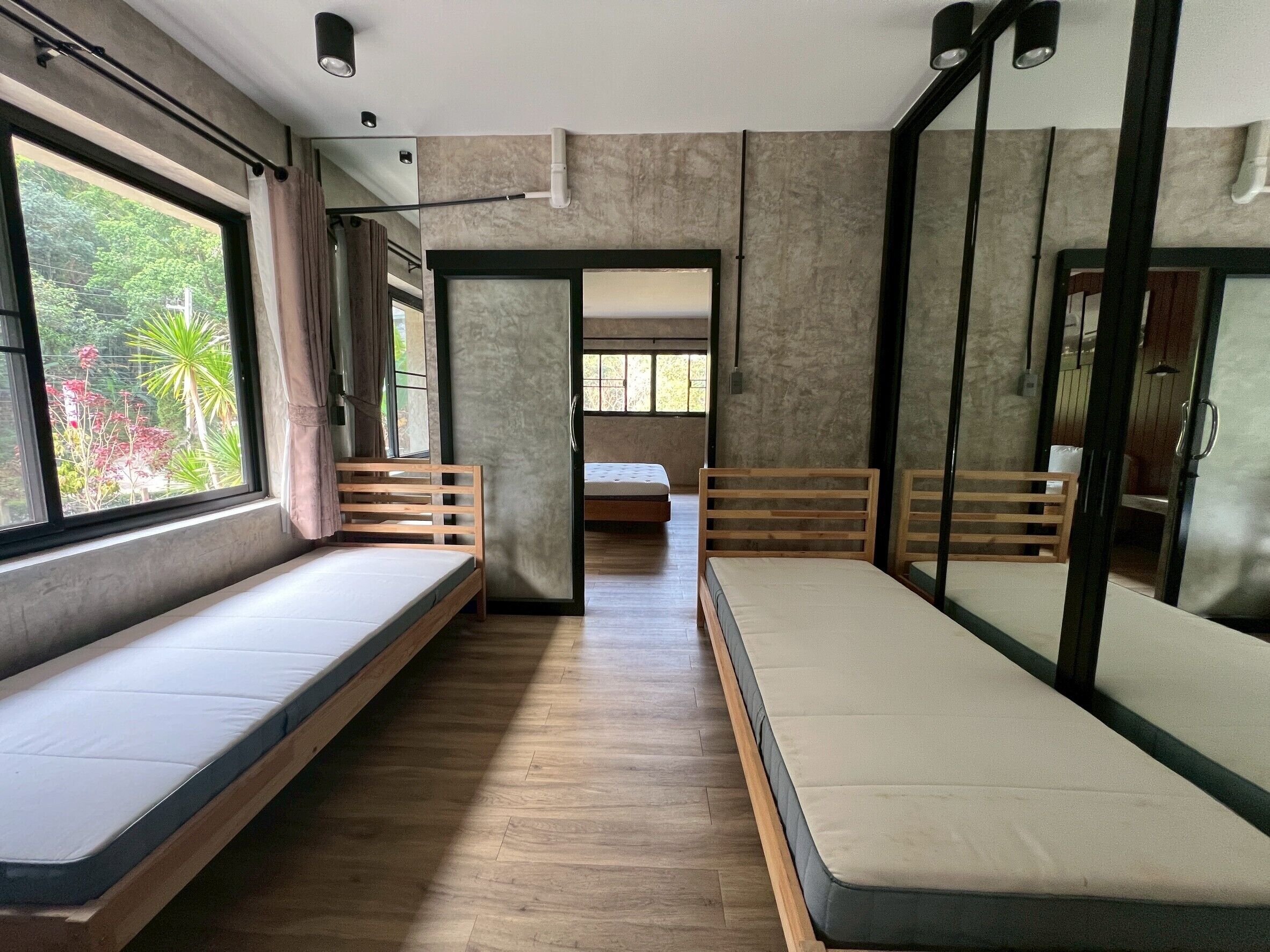 A room with two beds, a wooden bench, a mirror, and a window with a view of greenery.