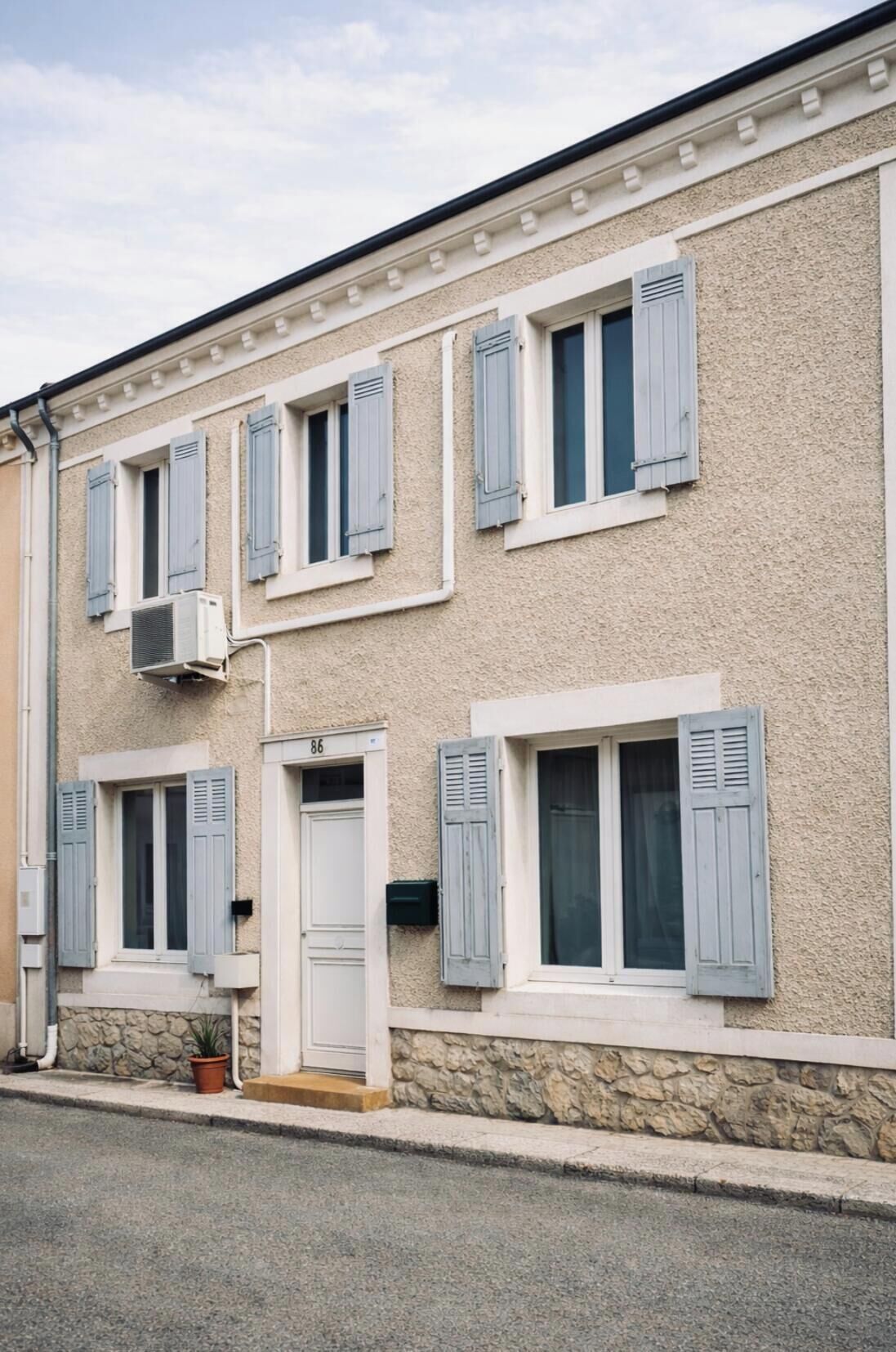 Un edificio de dos plantas con fachada de piedra, varias ventanas con contraventanas y una puerta blanca.