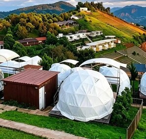 Paesaggio rurale con diverse strutture a forma di cupola, probabilmente adibite all'agricoltura, circondate da case e un terreno collinare.