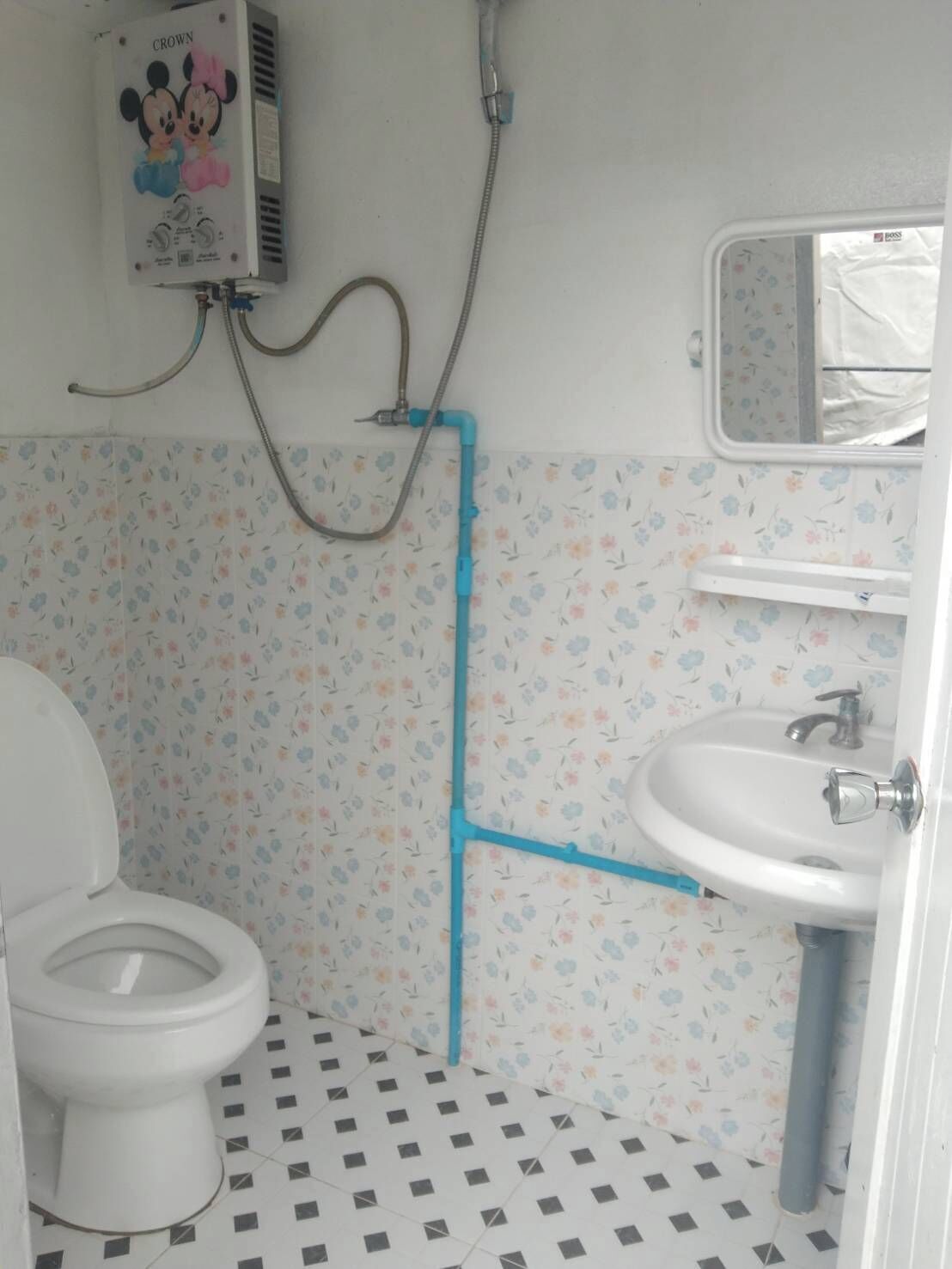 A bathroom with a toilet, a sink, a shower, and a Mickey Mouse poster on the wall.