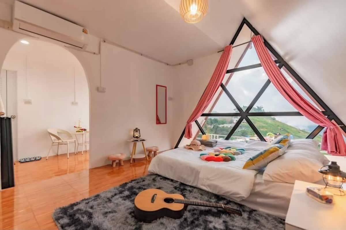 Un dormitorio con cama, una guitarra, una ventana con cortinas, un escritorio y una silla.