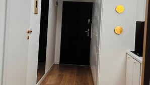 En hall med ett takfönster, trägolv, vita väggar och en svart dörr längst in.