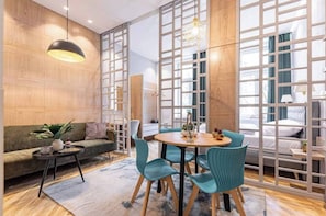 A modern hotel room with a wooden wall, a round dining table with chairs, a sofa, and a bed with a view. - The perfect cozy Oasis (Kraków)