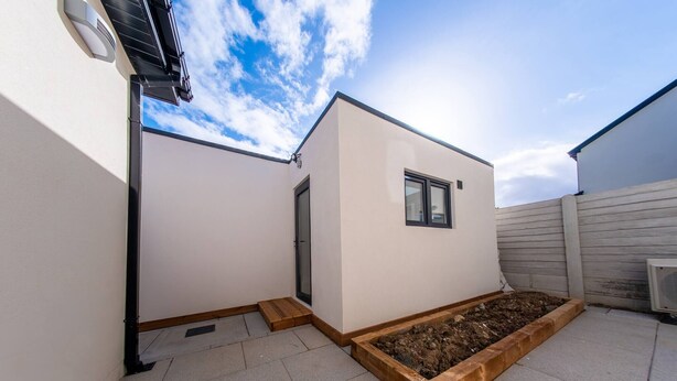 A modern building with a flat roof, a small window, and a raised garden bed.