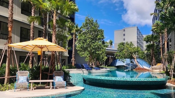 A pool area with lounge chairs, a sun umbrella, and palm trees. - Dcondo Reef  kathu Patong (Kathu)