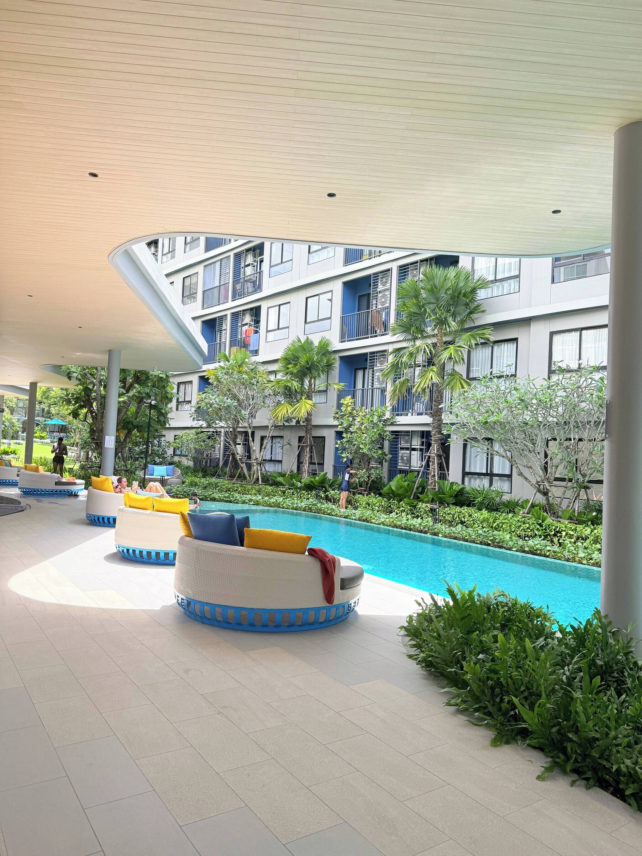 A poolside area with lounge chairs, a swimming pool, and a multi-story building with balconies.