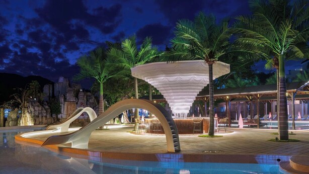 Un espace piscine doté d’un toboggan moderne, de palmiers et d’une structure conique originale.