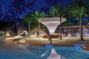 A pool area with a modern slide, palm trees, and a unique conical structure. - ZSZ Hot Spring Resort (Huizhou)