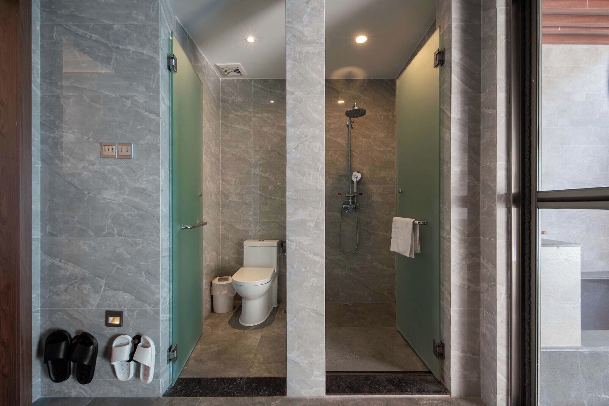 A modern bathroom with a shower, toilet, and slippers on the wall.