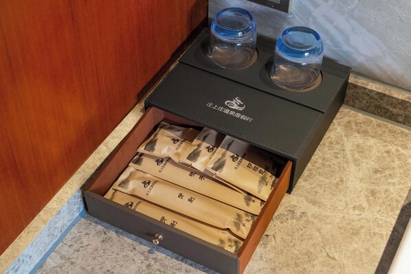 A drawer with multiple compartments containing items, a black box with a logo, and two clear glasses on top. - ZSZ Hot Spring Resort (Huizhou)
