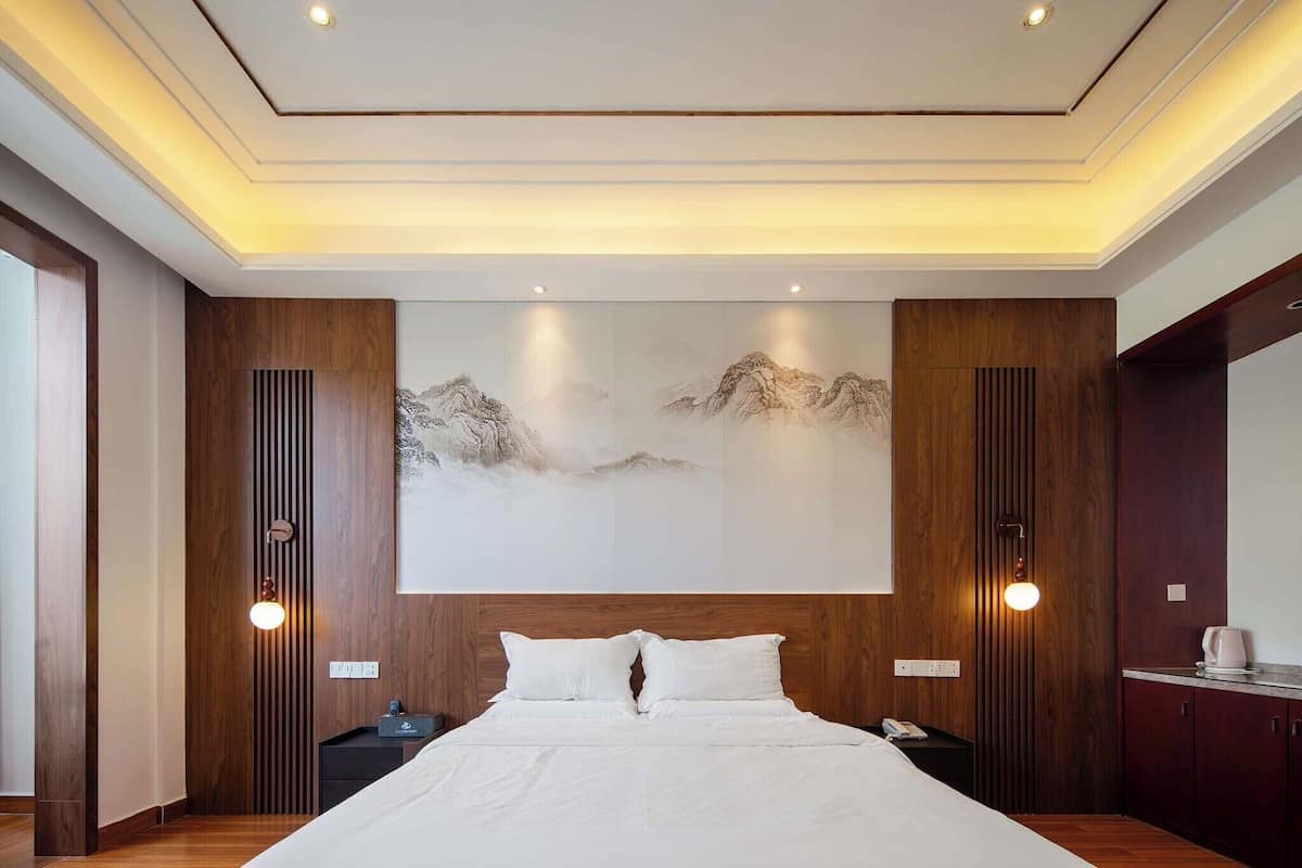 Une chambre d’hôtel moderne avec un grand lit, des panneaux de bois au mur, une œuvre d’art accrochée au mur et une table de chevet avec une lampe.