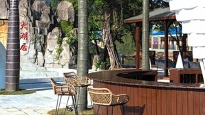 Un espace bar extérieur doté d’un comptoir en bois, de chaises en osier et d’une structure blanche en forme de tente.