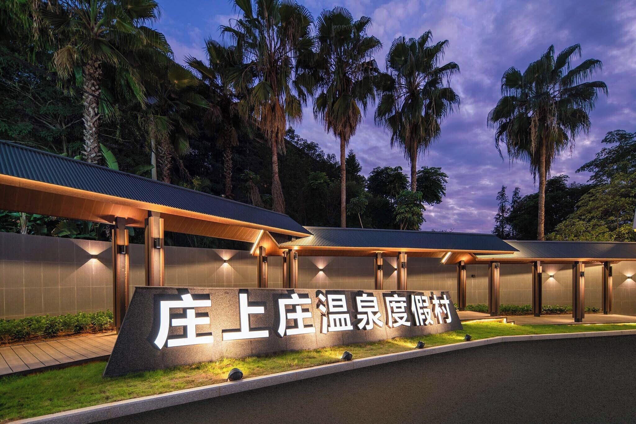 A modern building with a large sign, surrounded by palm trees and a well-lit entrance.