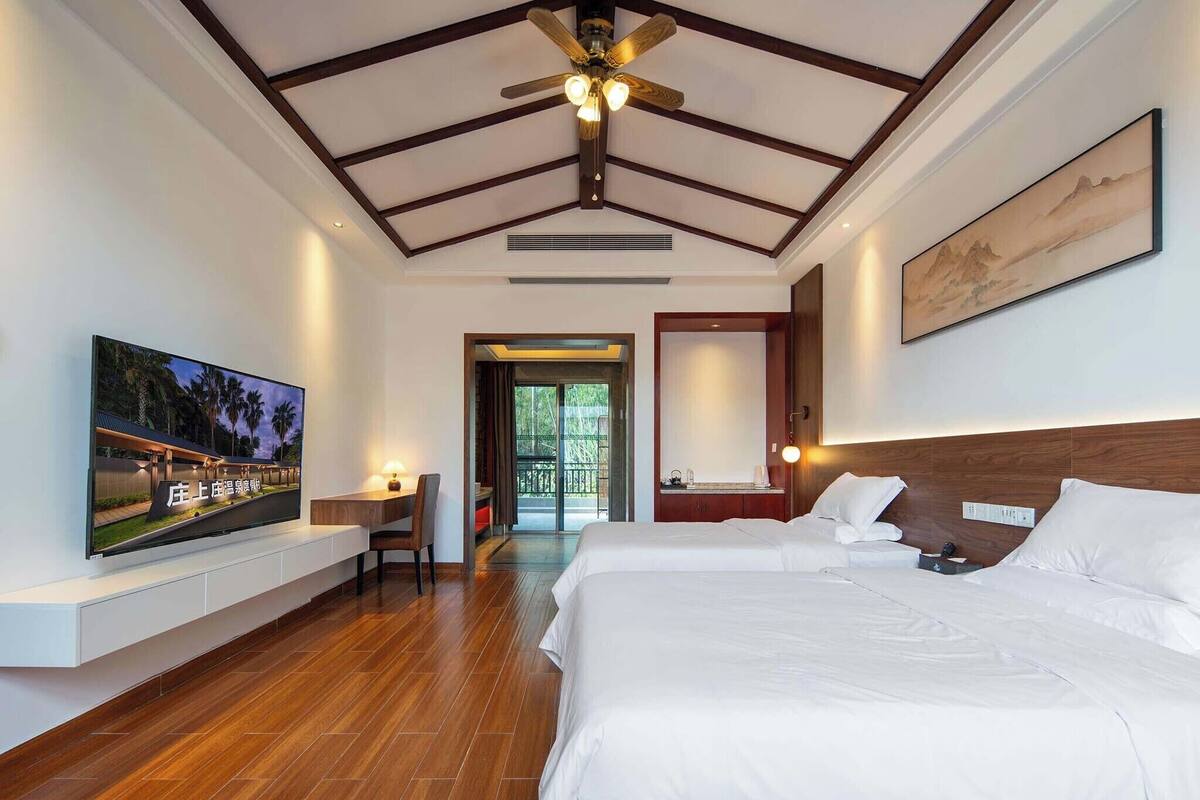 Une chambre d’hôtel avec un grand lit, un téléviseur à écran plat, un ventilateur de plafond et un plafond en bois.