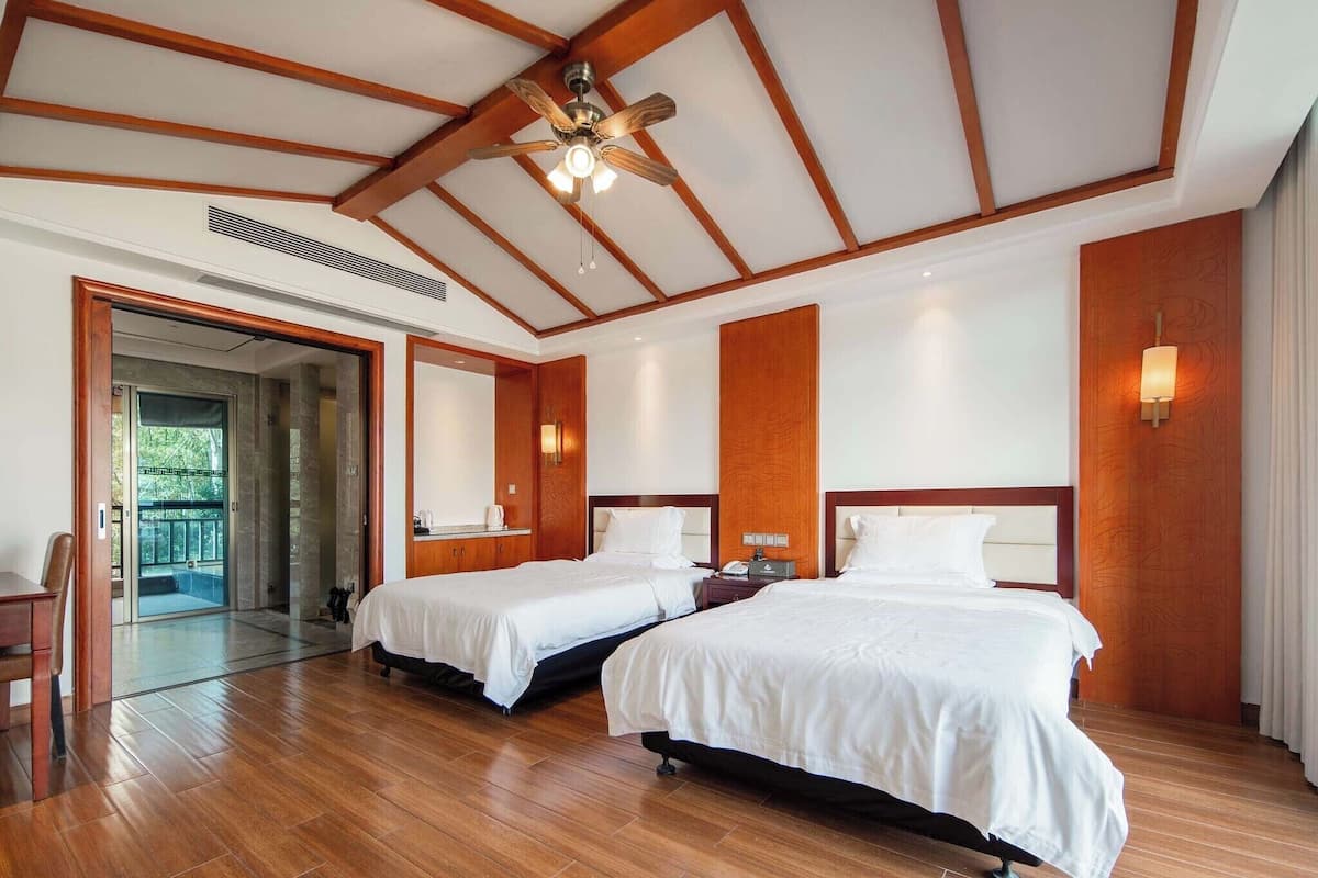 Une chambre d’hôtel avec deux lits, un plancher en bois, un ventilateur de plafond et une porte-fenêtre donnant sur un balcon.