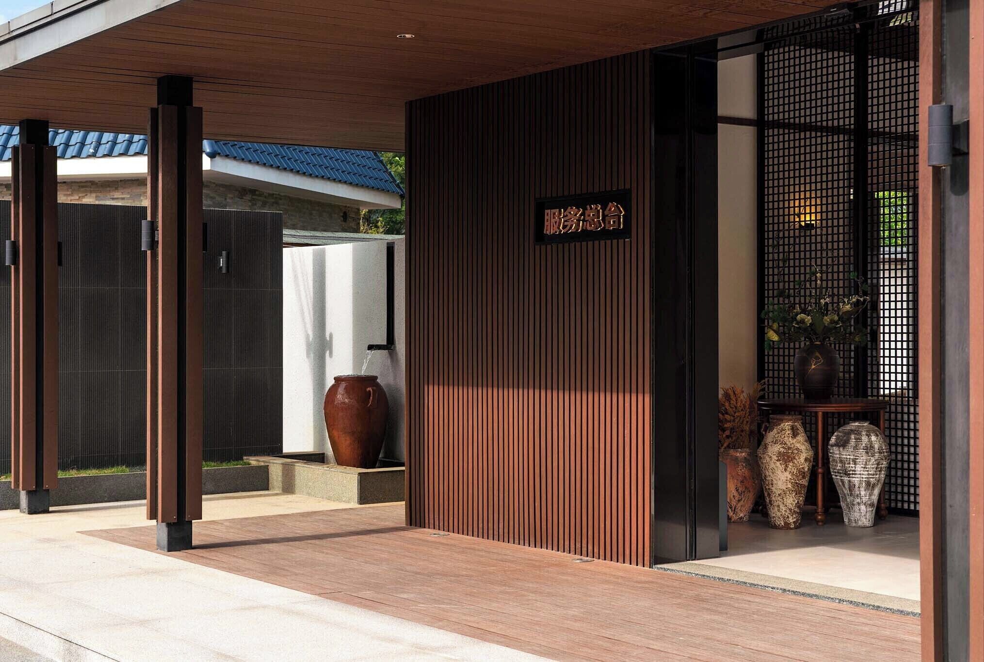 A modern building entrance with a wooden overhang, a signboard, and decorative vases.