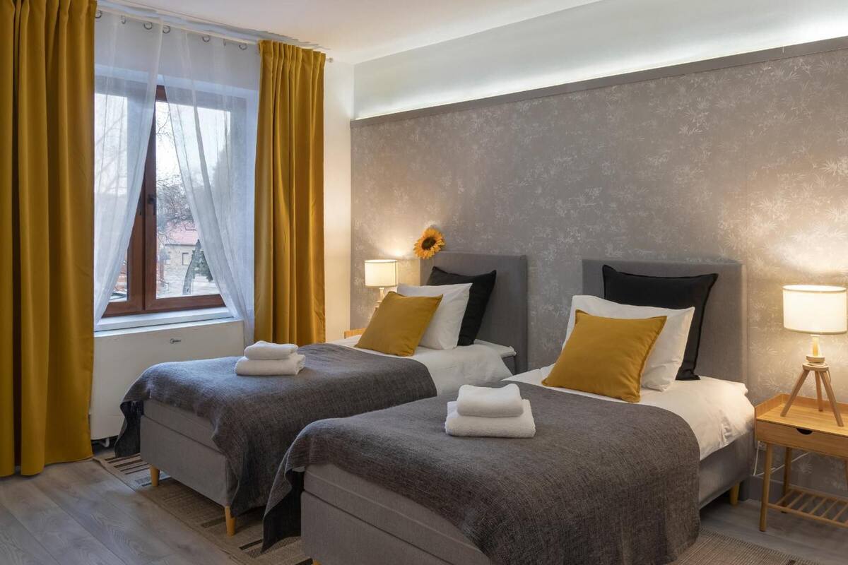 A hotel room with two beds, a window with curtains, a bedside lamp, and a sunflower decoration.