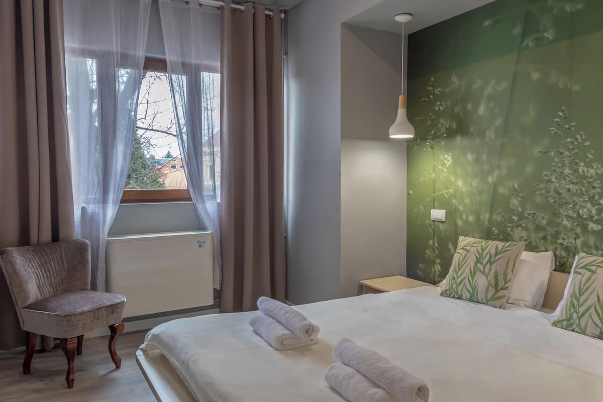 A bedroom with a bed, a chair, a window with curtains, and a wall with a leaf pattern.