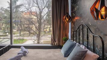 A bedroom with a large window, a bed, a nightstand, and a hanging light fixture.