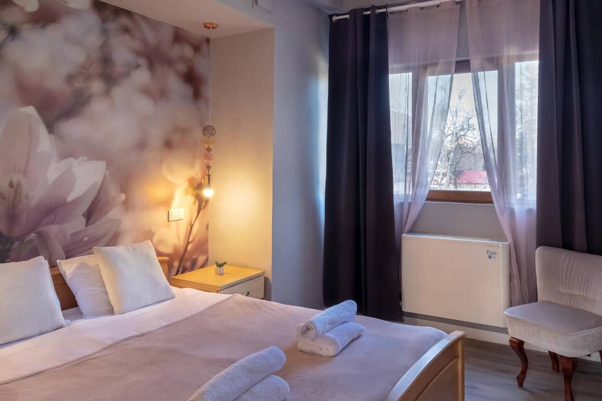 A hotel room with a bed, a chair, a nightstand, a lamp, and a window with curtains.