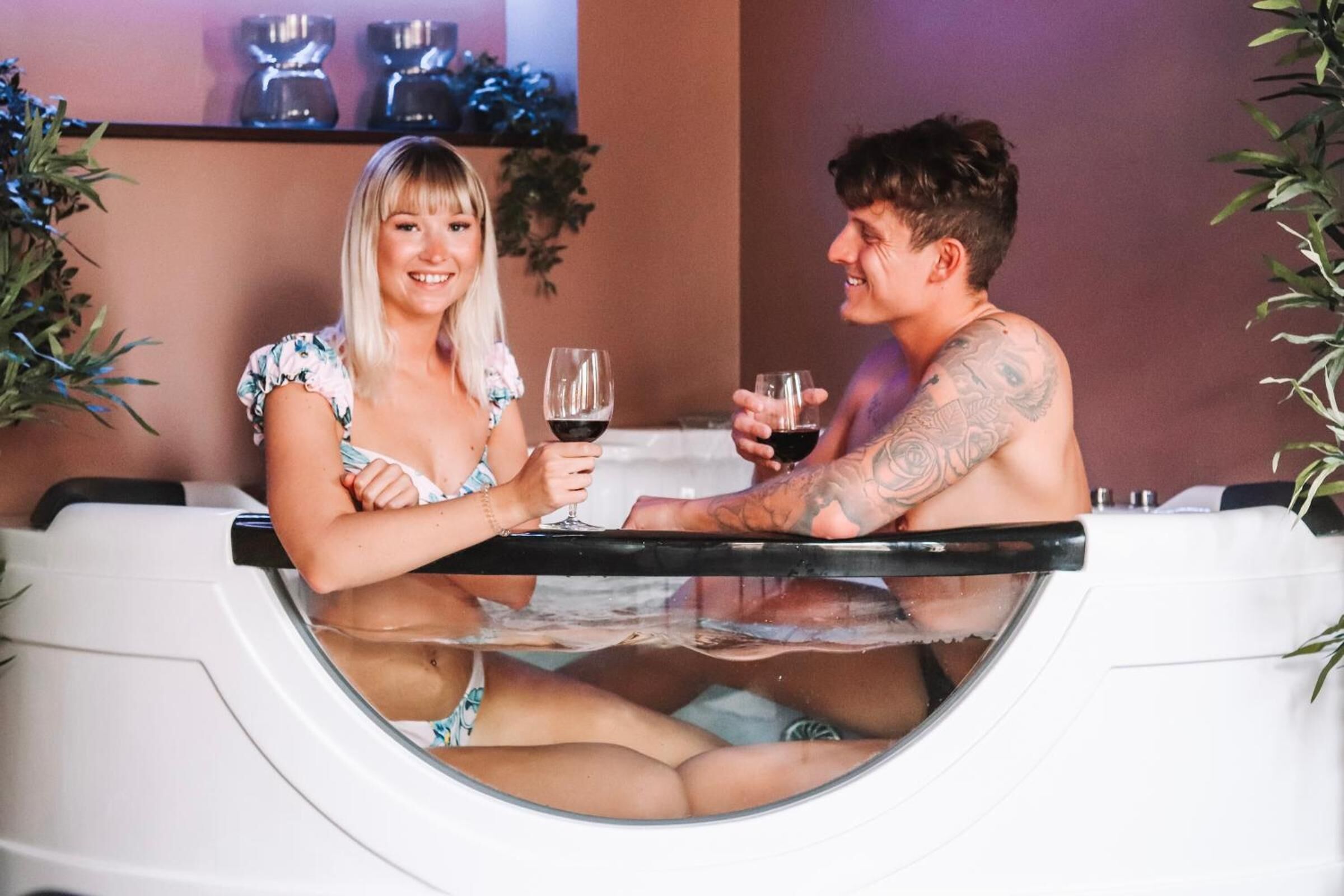 Ein Paar in einer Badewanne mit Glasabtrennung, umgeben von Zimmerpflanzen.