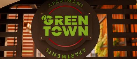 A circular sign with 'GREEN TOWN' and 'APARTMANS' text, mounted on a metal structure.