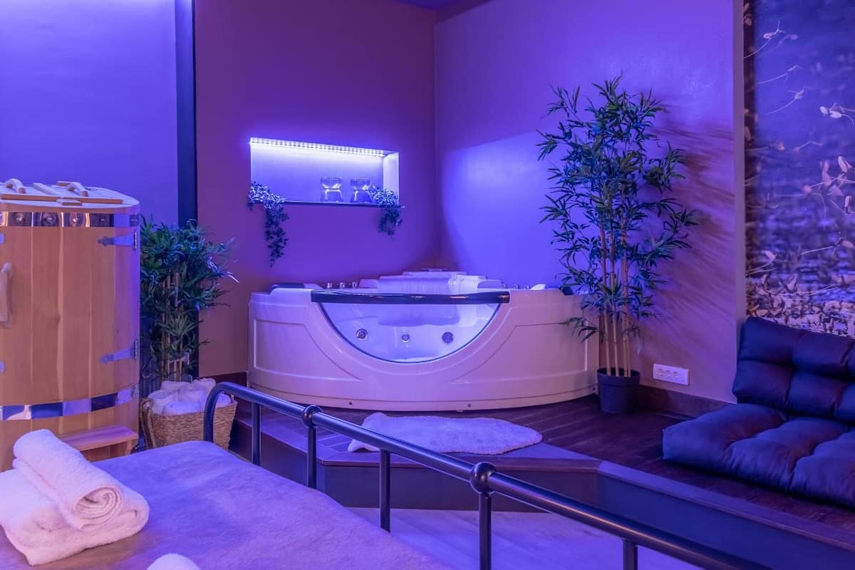 A spa room with a hot tub, wooden cabinet, and a massage table.