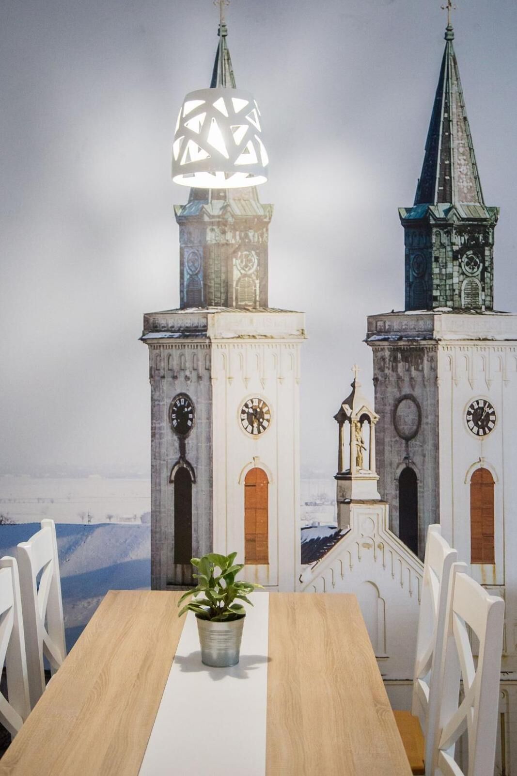 Ein Esstisch mit Stühlen, einer Topfpflanze und einem Wandbild von zwei Kirchtürmen.