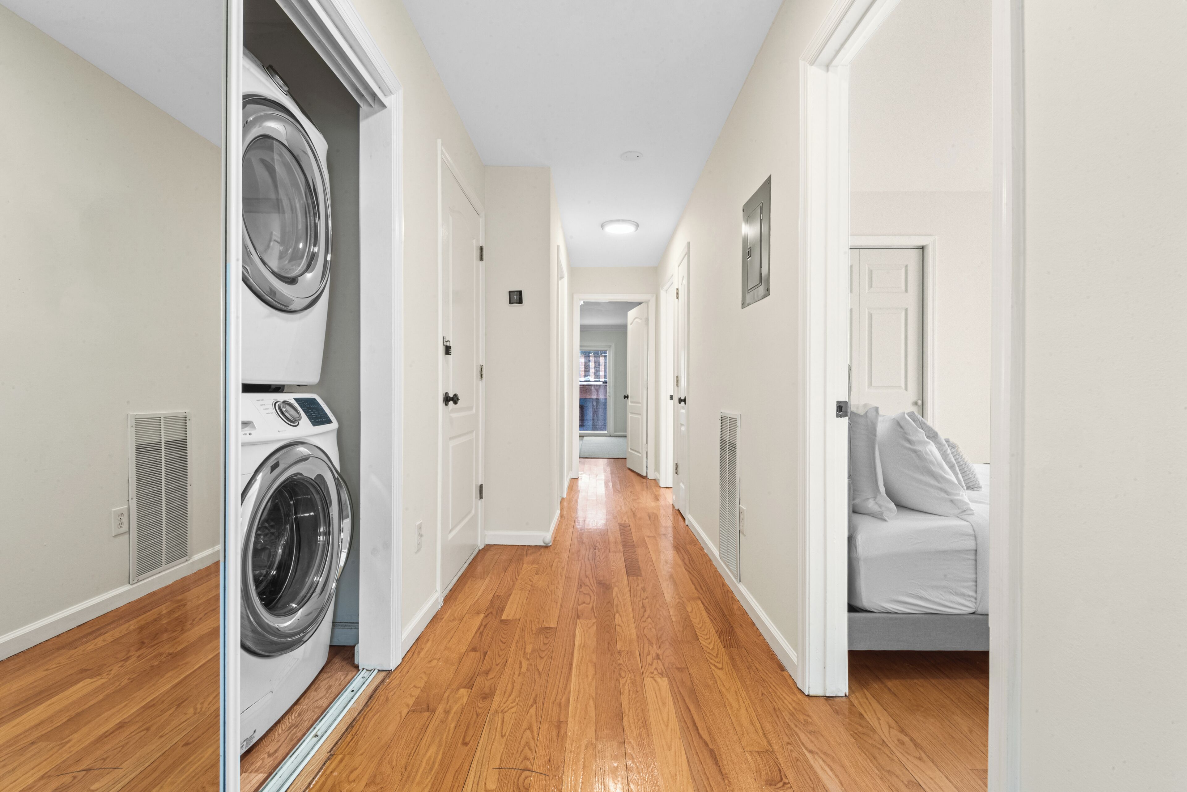 A hallway with a washing machine, a bed, and a door leading to another room.