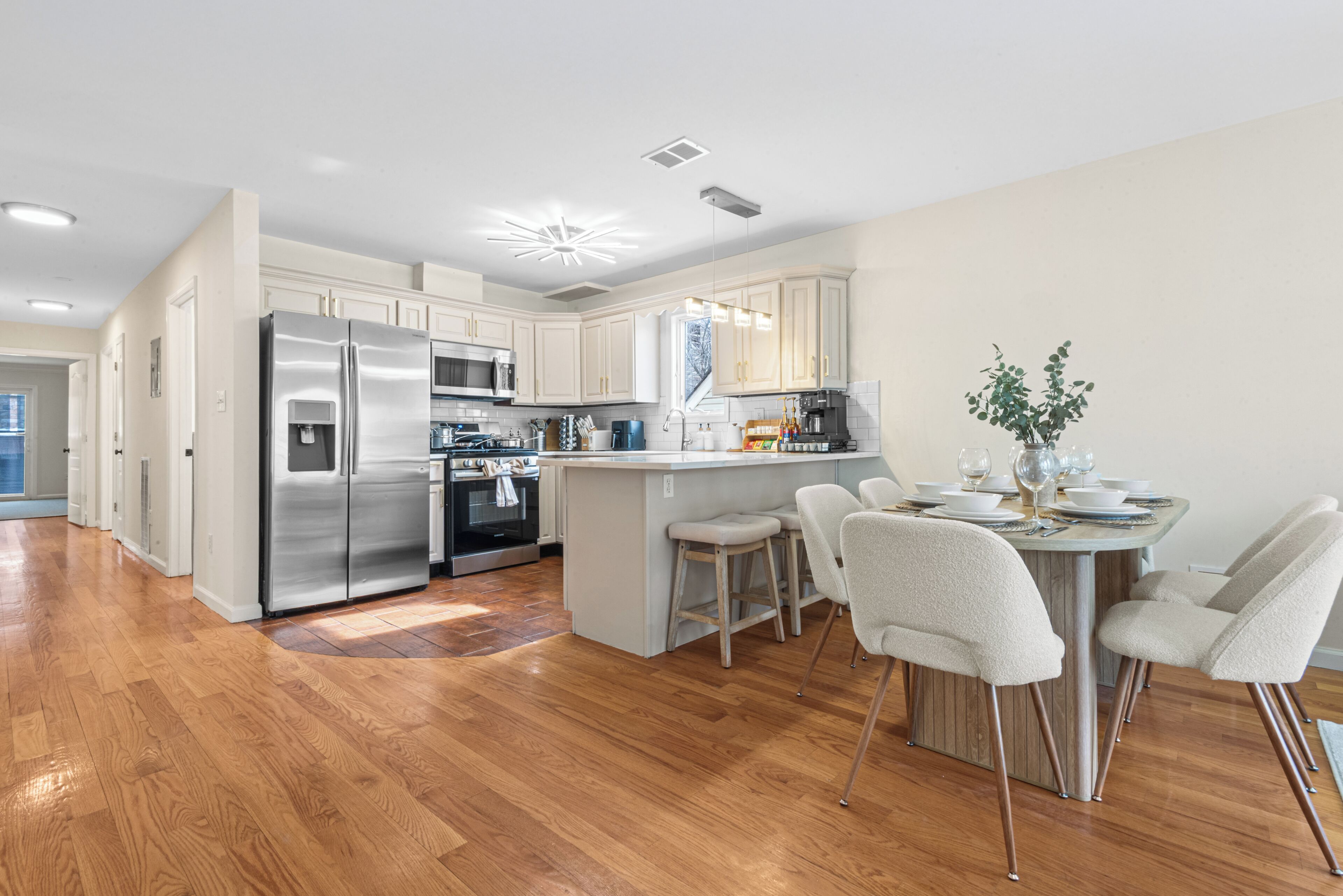 A modern kitchen with stainless steel appliances, a central island with bar stools, and wooden flooring.