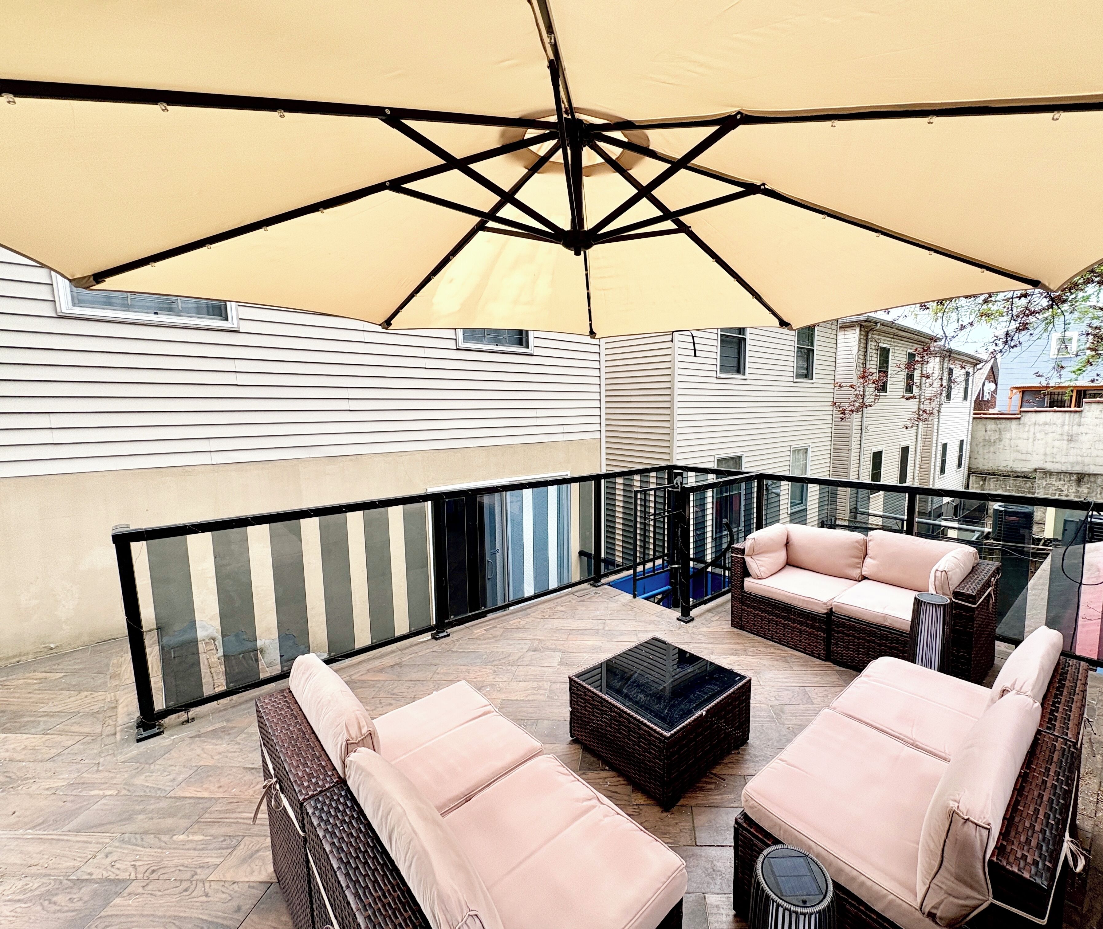 A rooftop patio with outdoor furniture, a large umbrella, and a view of neighboring buildings.